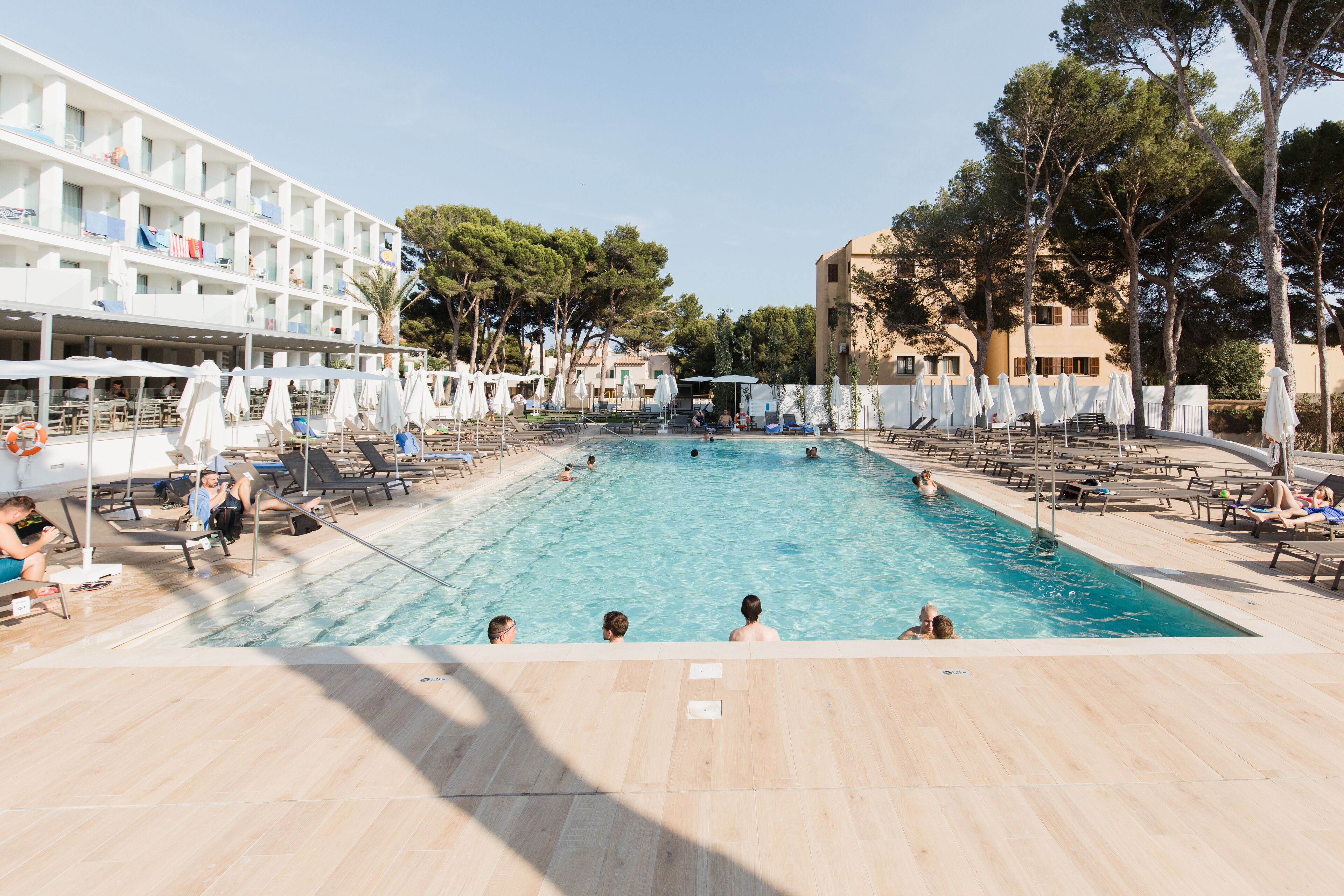 A swimming pool with lounge chairs and umbrellas, surrounded by a hotel building with multiple floors and balconies.