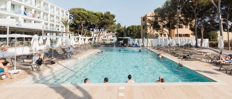 A swimming pool with lounge chairs and umbrellas, surrounded by a hotel building with multiple floors and balconies.