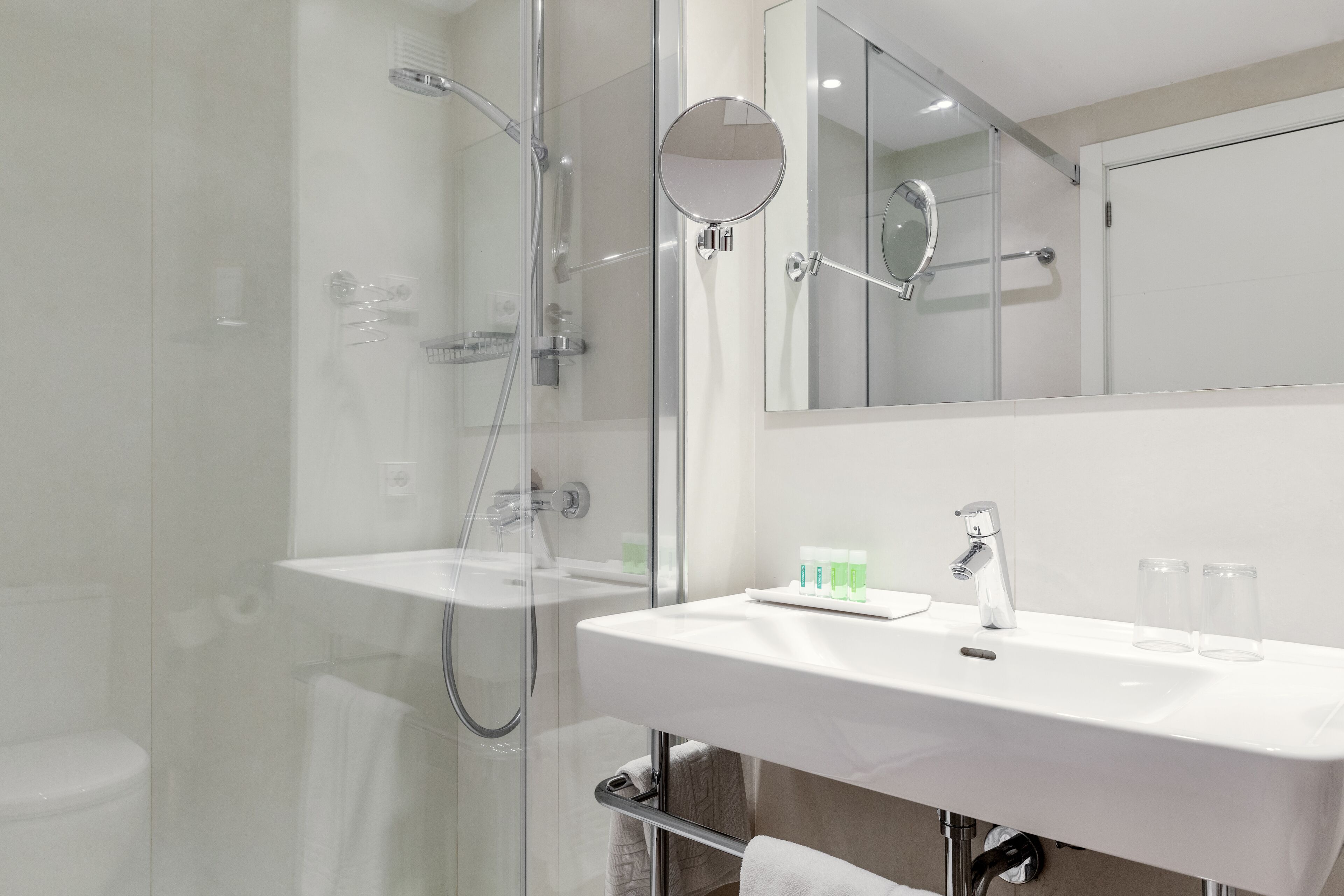 Een moderne badkamer met een douchecabine van glas, een wit wastafelmeubel en een grote spiegel.