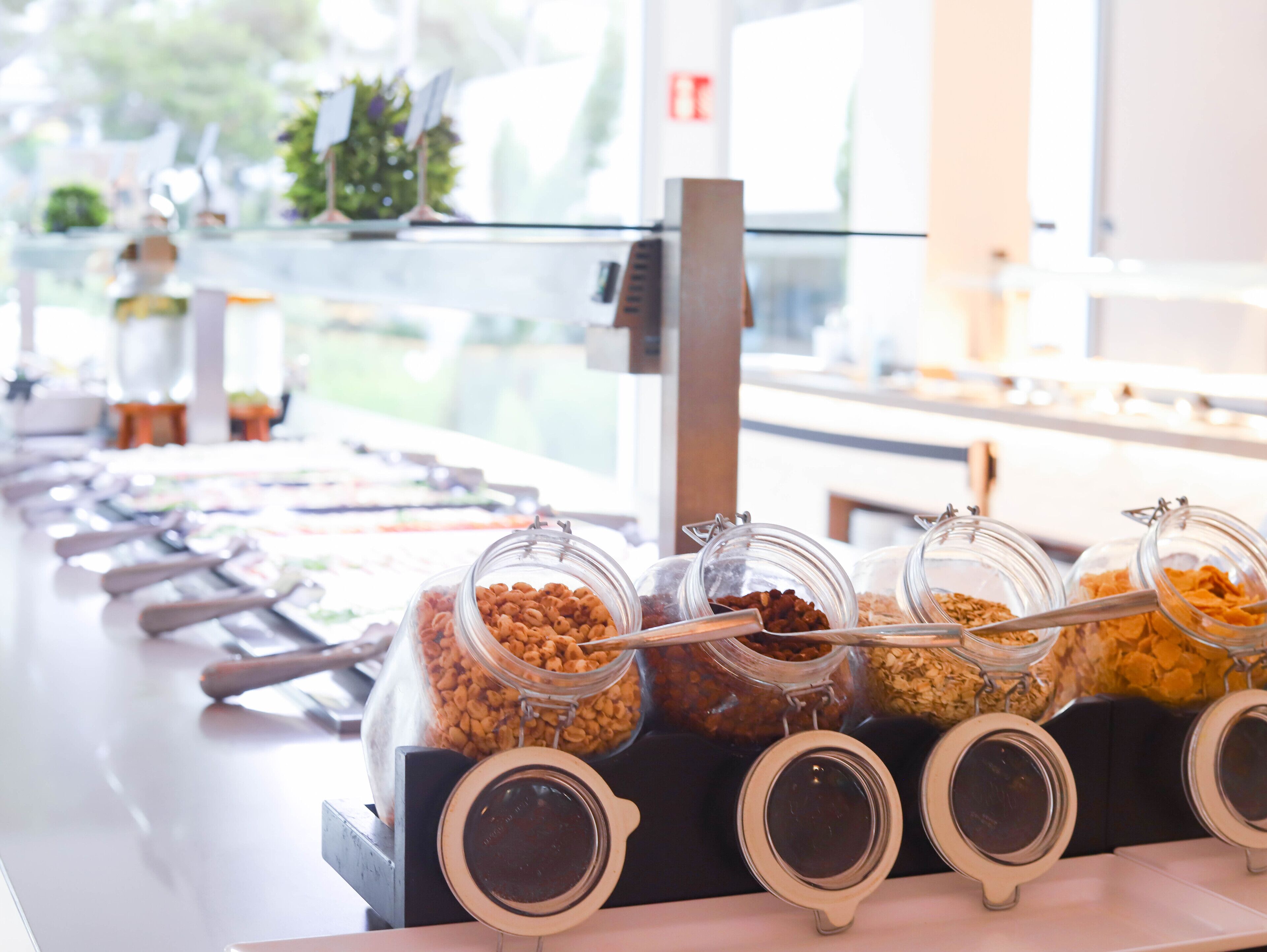 Un bufet amb diversos aliments en recipients de vidre, disposats sobre un taulell amb utensilis per servir.