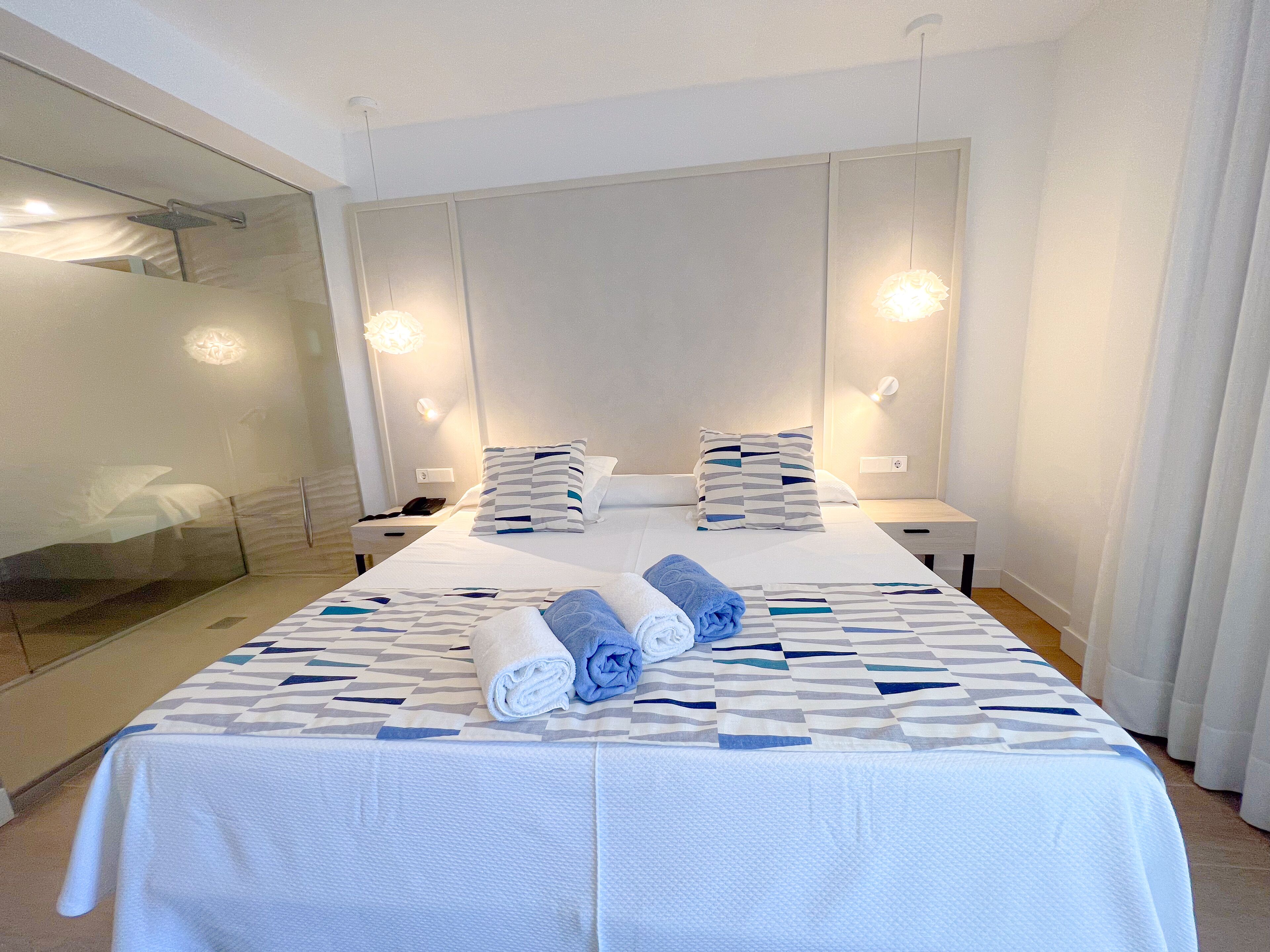 Een hotelkamer met een groot bed, twee nachtkastjes, een douchecabine van glas en een moderne lamp.