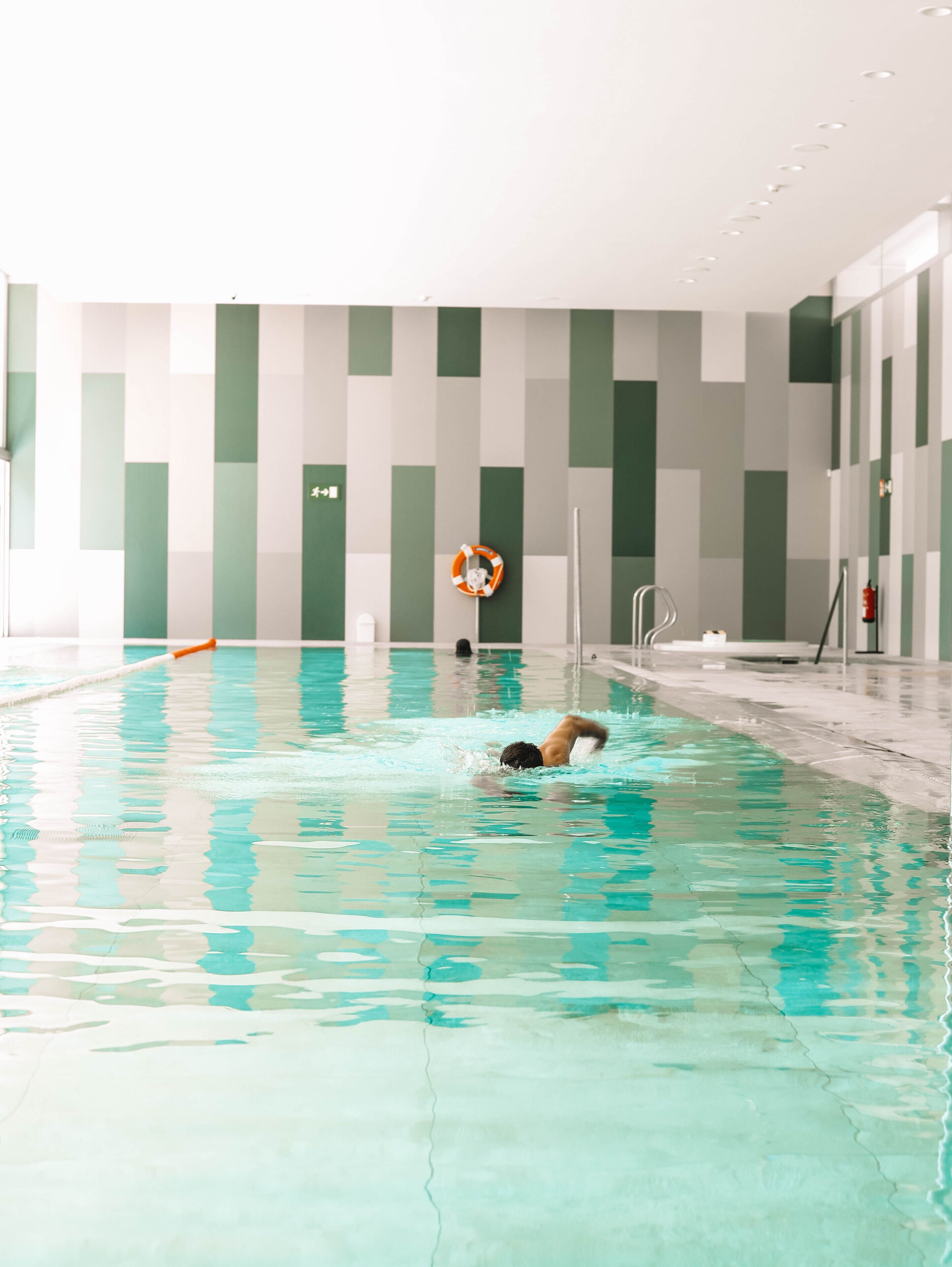 An indoor swimming pool with clear water, a lifebuoy, and a pool ladder.