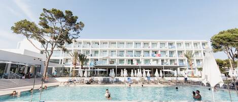 A hotel pool area with sun loungers, umbrellas, and a building with balconies.