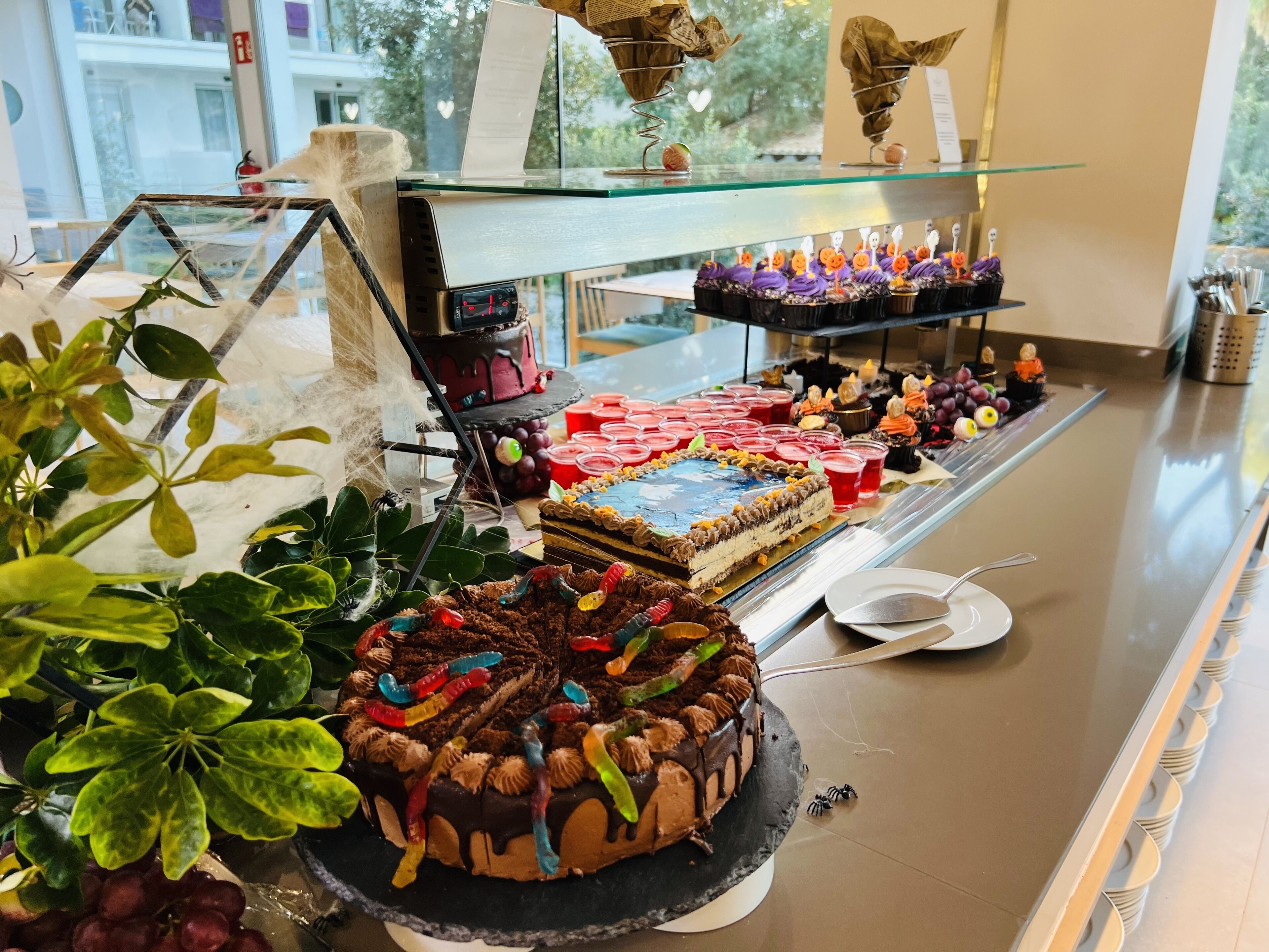 A dessert display with various cakes and pastries, including a large chocolate cake with gummy worms and a smaller cake with a blue topping.