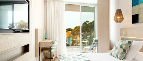 A modern hotel room with a large bed, a desk with chairs, a television, and a balcony with a view of the city.
