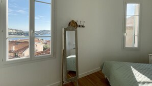 Une chambre avec une grande fenêtre, un lit, un miroir et une petite table.