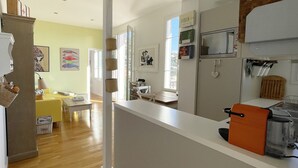Une cuisine moderne avec des meubles blancs, une machine à café et un grille-pain. On y trouve également un coin repas avec un canapé jaune et une table.