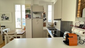 Une cuisine moderne avec des armoires blanches, un four encastré et un évier. On y trouve une table à manger avec des chaises, ainsi qu’une fenêtre qui laisse entrer la lumière naturelle.