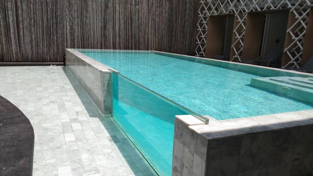 A rectangular swimming pool with clear blue water, surrounded by a tiled deck and a wooden fence. - Yanud Residence (Ratsada)