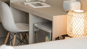 A hotel room with a wooden desk, a white chair, a minibar, a round mirror, a wall socket, and a lamp. - Yanud Residence (Ratsada)