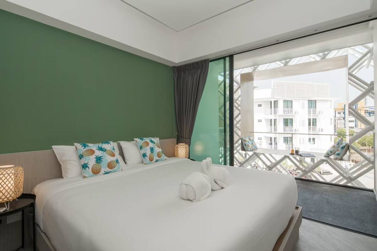 A hotel room with a large bed, green walls, and a view of buildings through a window with a geometric frame.