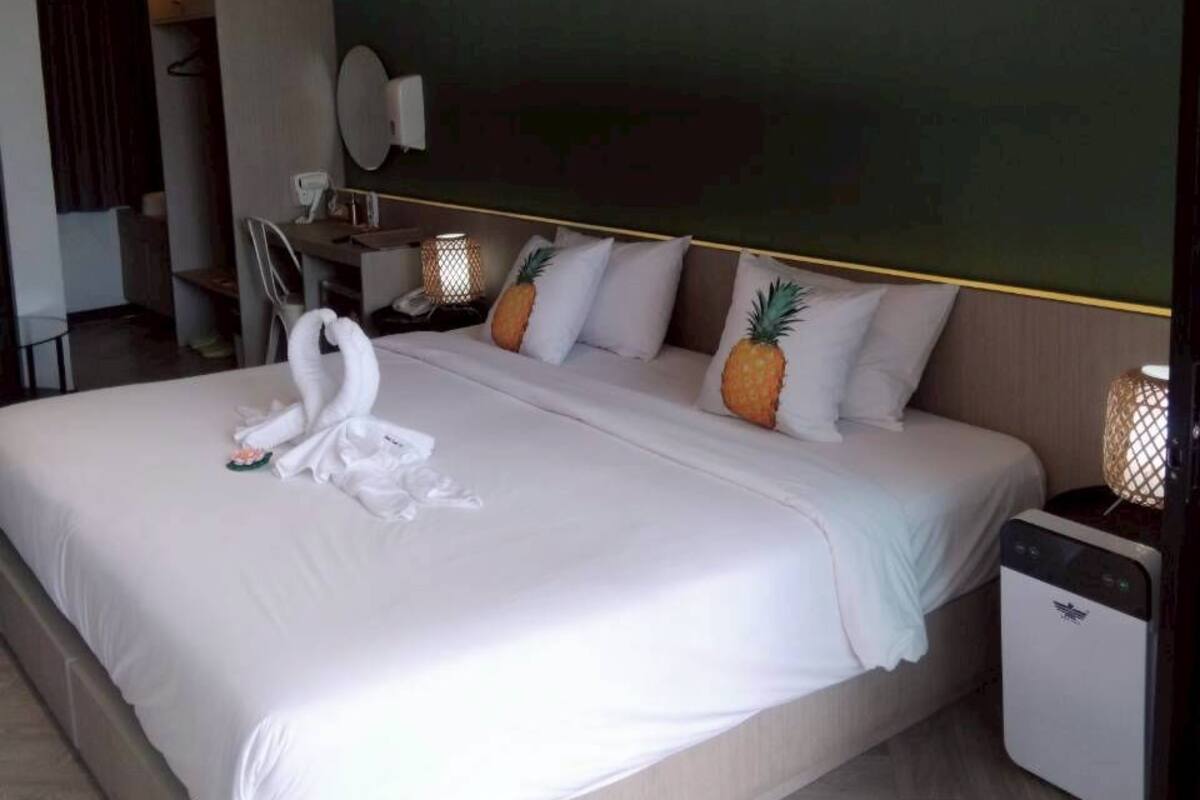 A hotel room with a large bed, a bedside table, a lamp, and an air conditioning unit.