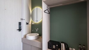 A modern bathroom with a white sink, a mirror with a circular light, a black safe, and a kettle on the counter. - Yanud Residence (Ratsada)