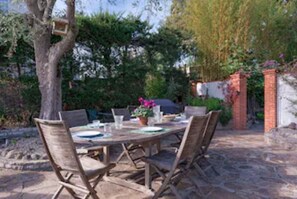 An outdoor dining area with a stone table and wooden chairs, surrounded by greenery and a brick wall. - Charming Villa,  Sea View,  minutes from Palm Beach and Cannes (Vallauris)