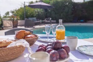 A breakfast setup with croissants, plums, a glass of orange juice, and a bottle of orange juice by a poolside. - Charming Villa,  Sea View,  minutes from Palm Beach and Cannes (Vallauris)