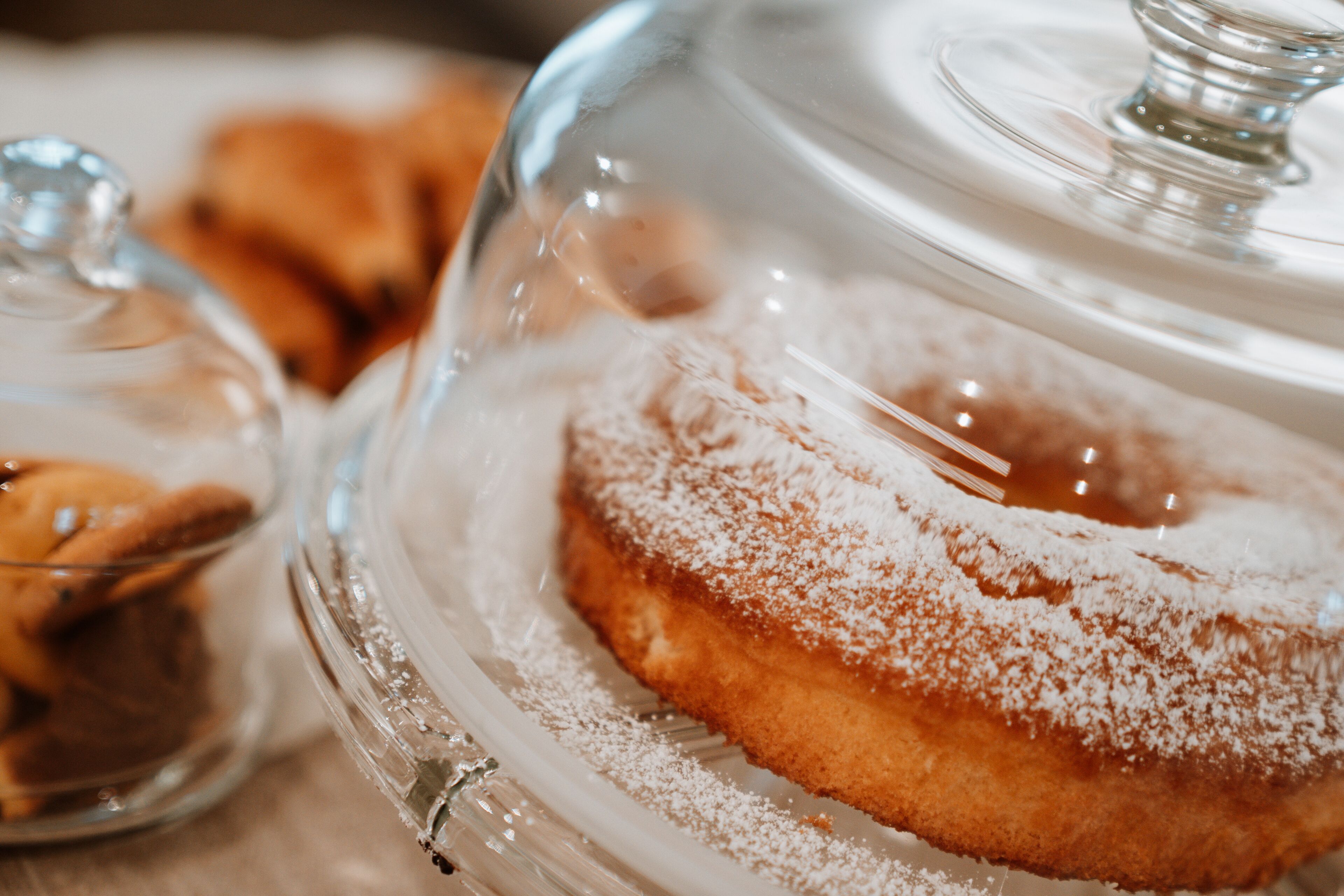 Un beignet glacé saupoudré de sucre glace, posé sur un présentoir en verre transparent.