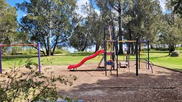 A playground with a red slide and climbing structures, surrounded by trees and a grassy area.