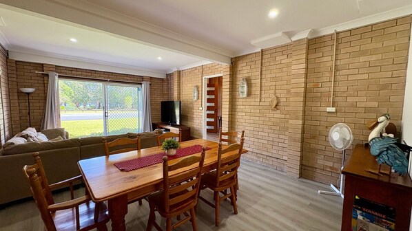 A cozy living room with a wooden dining table, chairs, a sofa, and a TV.