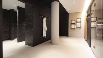 Un baño moderno con paredes de mármol, un pilar blanco grande y puertas de ducha de cristal.