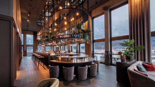A modern bar with a circular design, multiple seating areas, and large windows offering a city view.