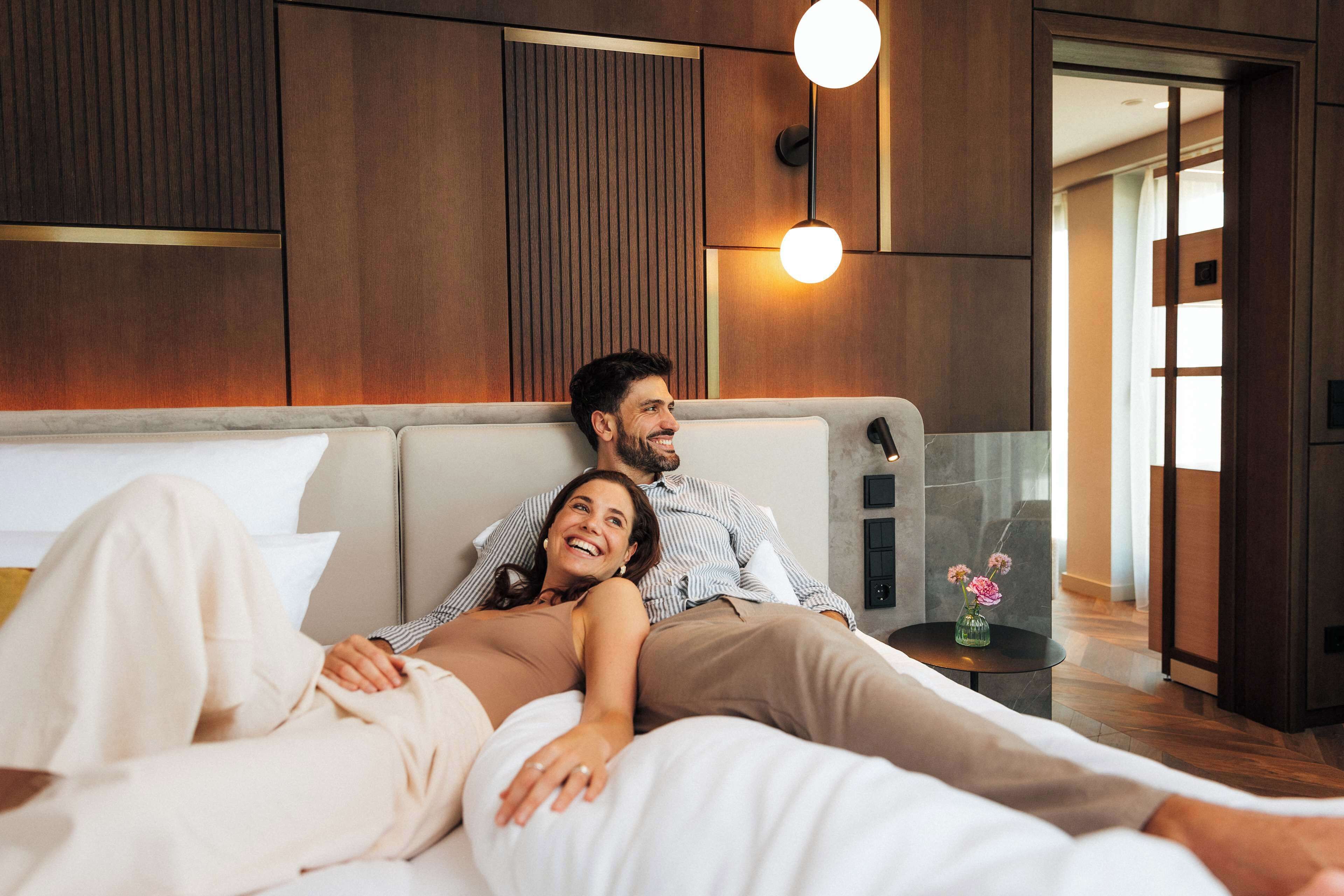 A modern bedroom with a large bed, wooden paneling on the walls, and a small side table with a vase.