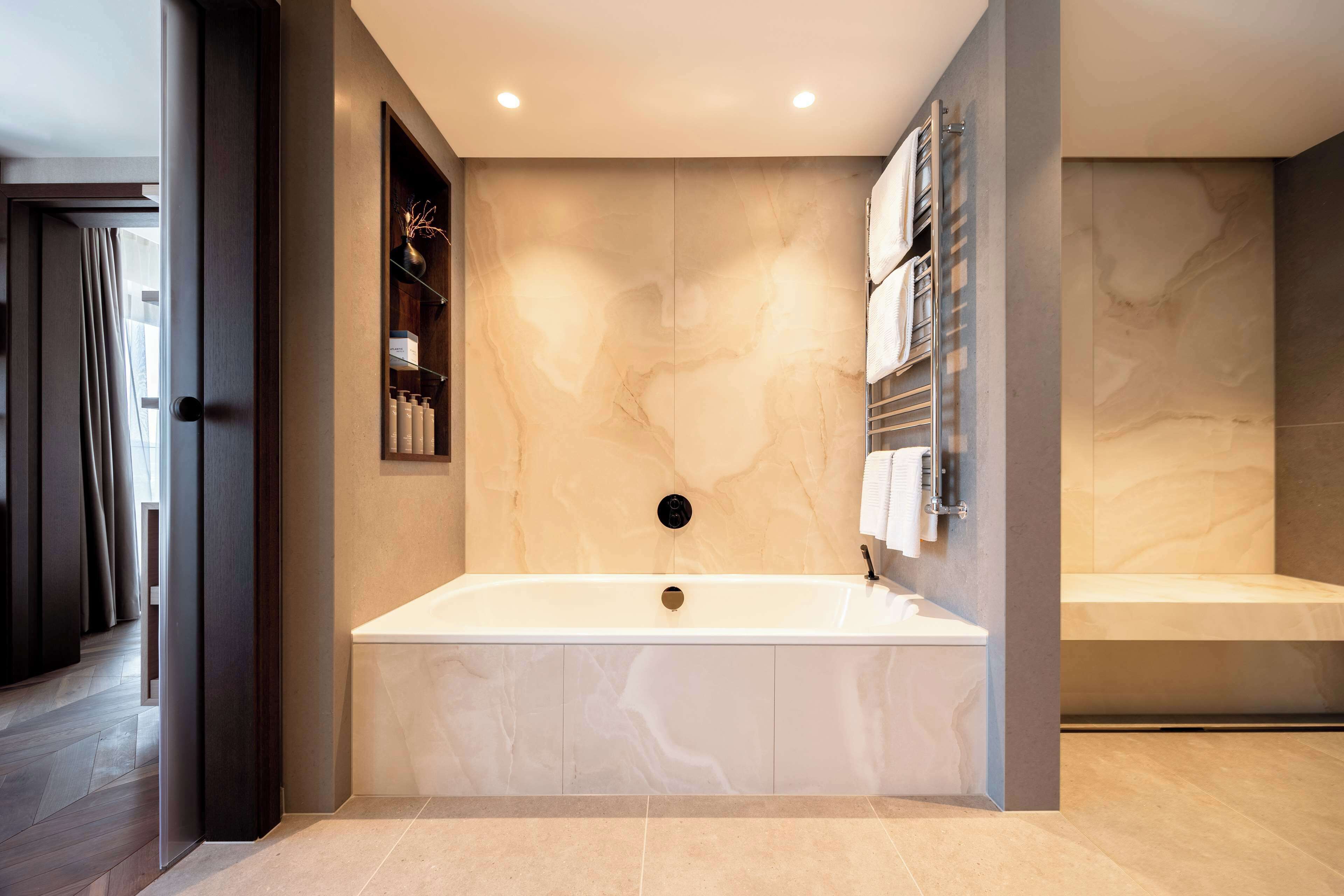 Een moderne badkamer met een vrijstaand bad, marmeren wanden en een inbouwkastje met toiletartikelen.