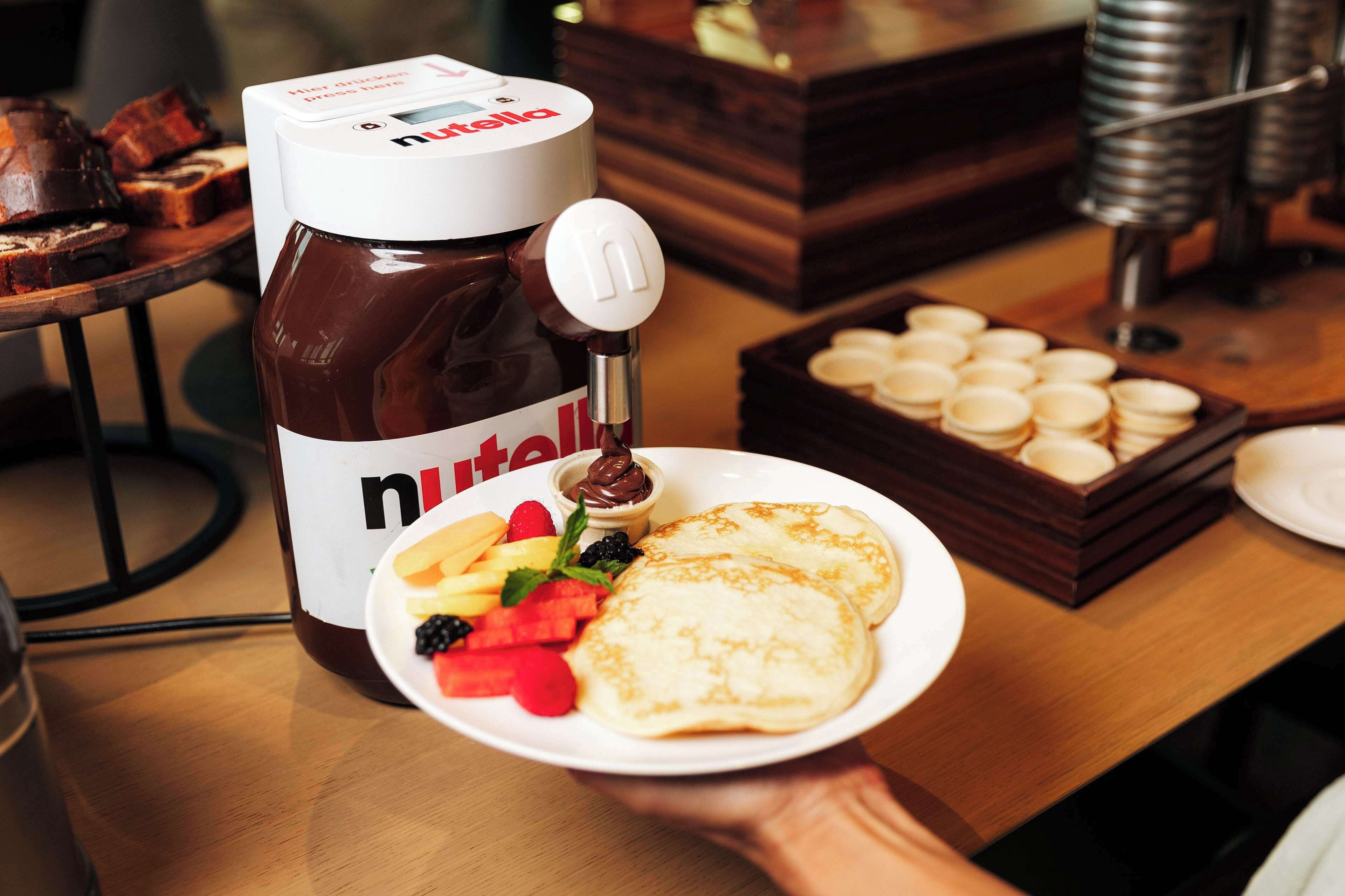 Ein Nutella-Spender mit einem Teller Pfannkuchen und frischem Obst.