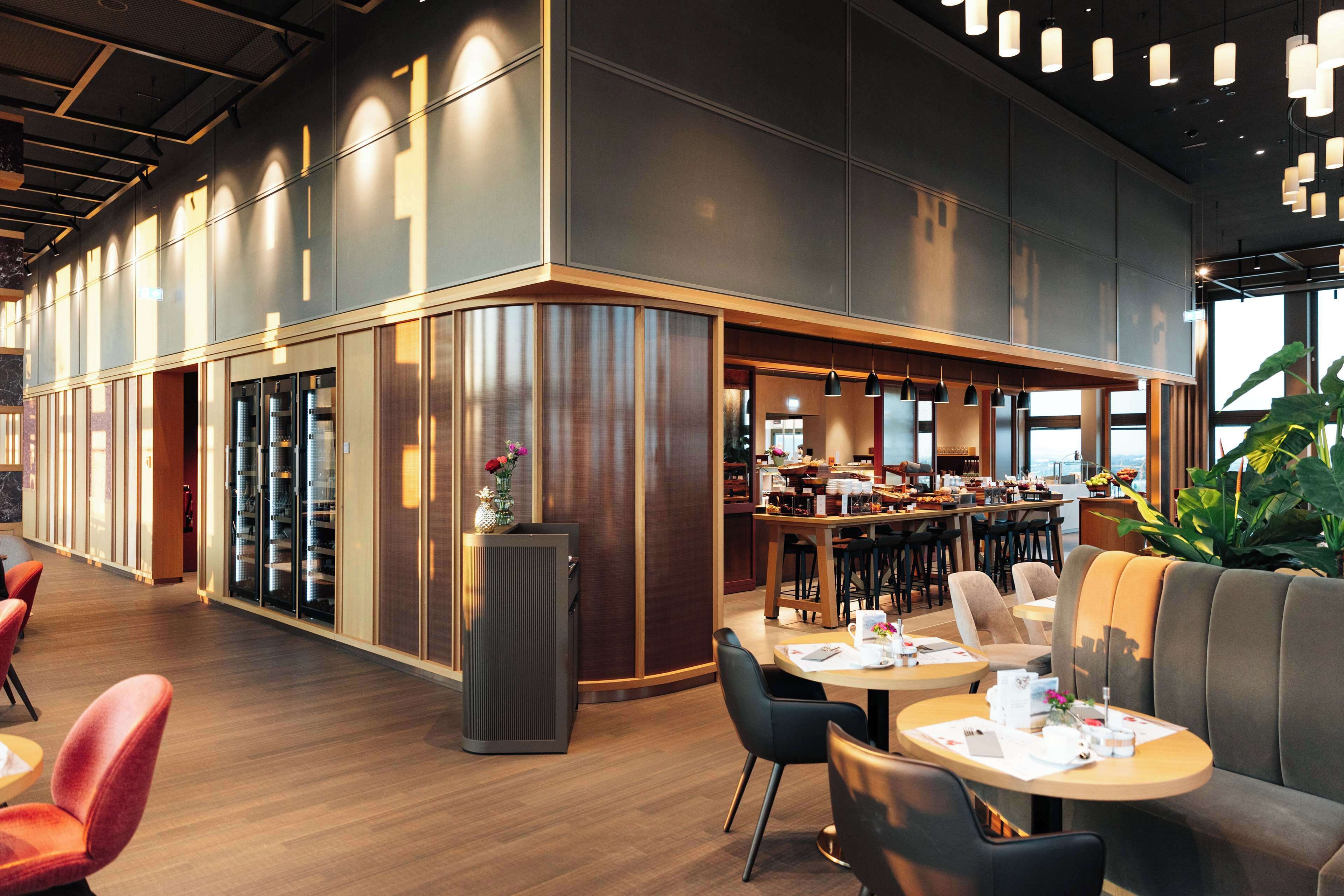 Ein modernes Restaurant mit einer langen Theke, mehreren Sitzbereichen und großen Fenstern.