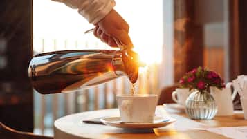 Une main verse du café dans une tasse posée sur une table, à côté d’un vase de fleurs et d’un menu.