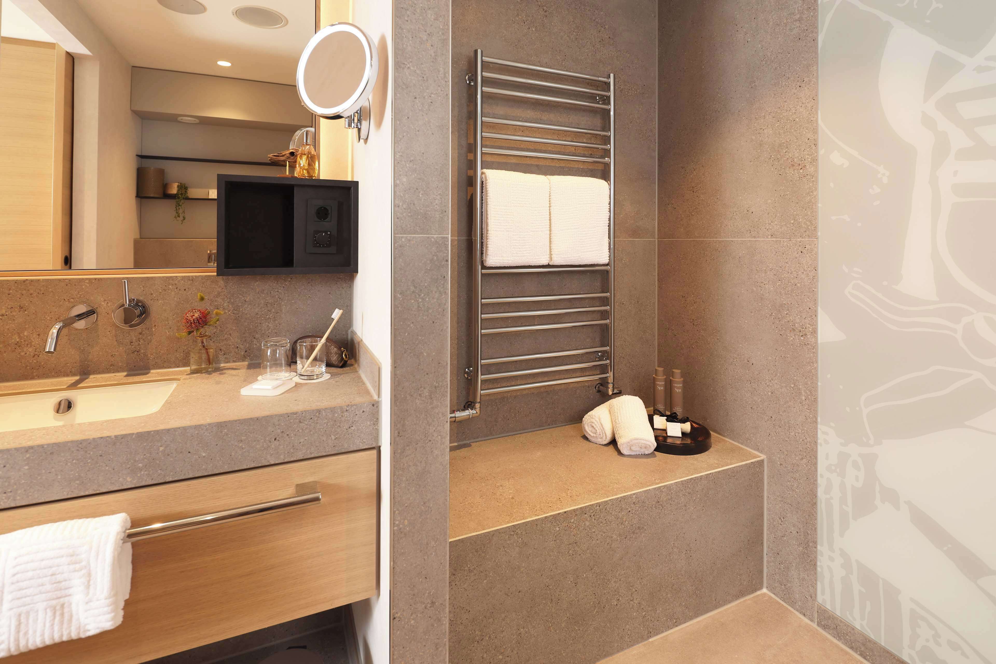 A modern bathroom with a vanity, sink, mirror, towel rack, and a heated towel rail.