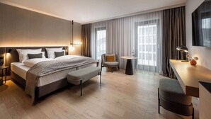 A modern hotel room with a large bed, a desk, a chair, and a small table.