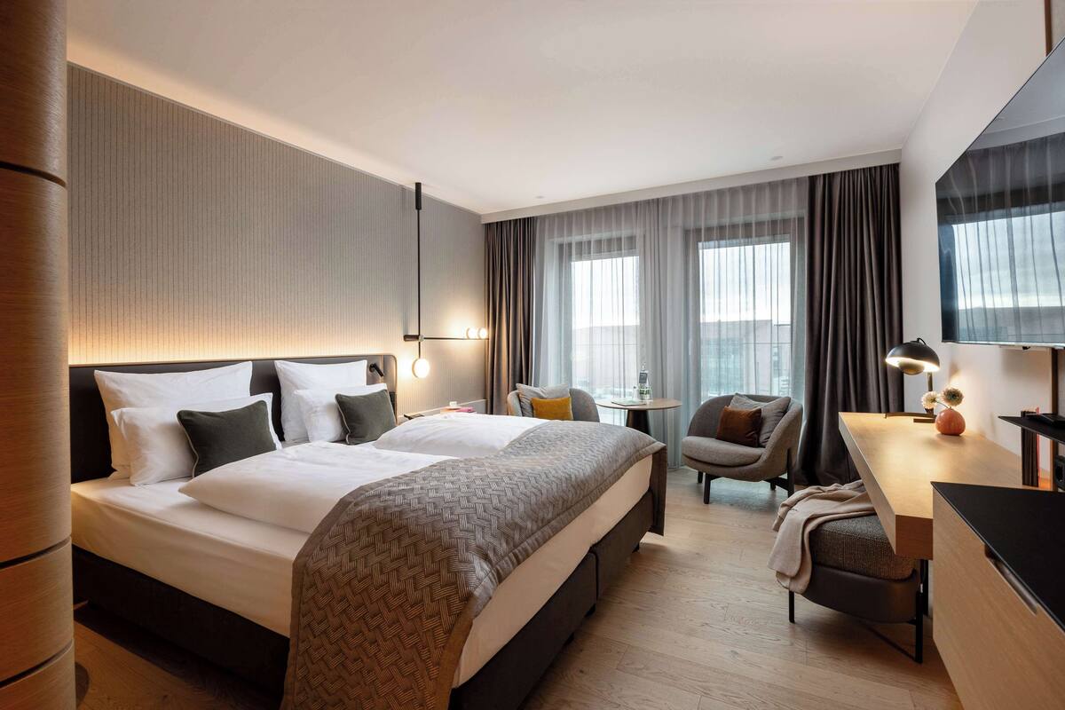 A modern hotel room with a large bed, a desk, a chair, and a TV.