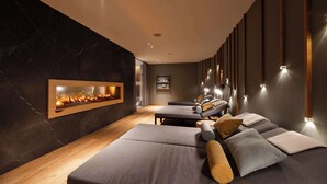 A modern spa room with a fireplace, massage chairs, and ambient lighting.