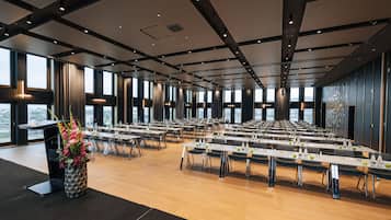 Un salón de conferencias con varias mesas y sillas, ventanas amplias y un diseño moderno de techo.