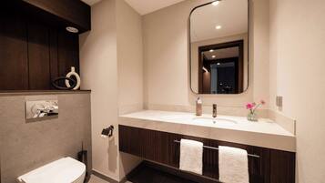 Un baño moderno con un inodoro blanco, un espejo grande, un tocador con lavabo y dos toallas colgadas en un perchero.