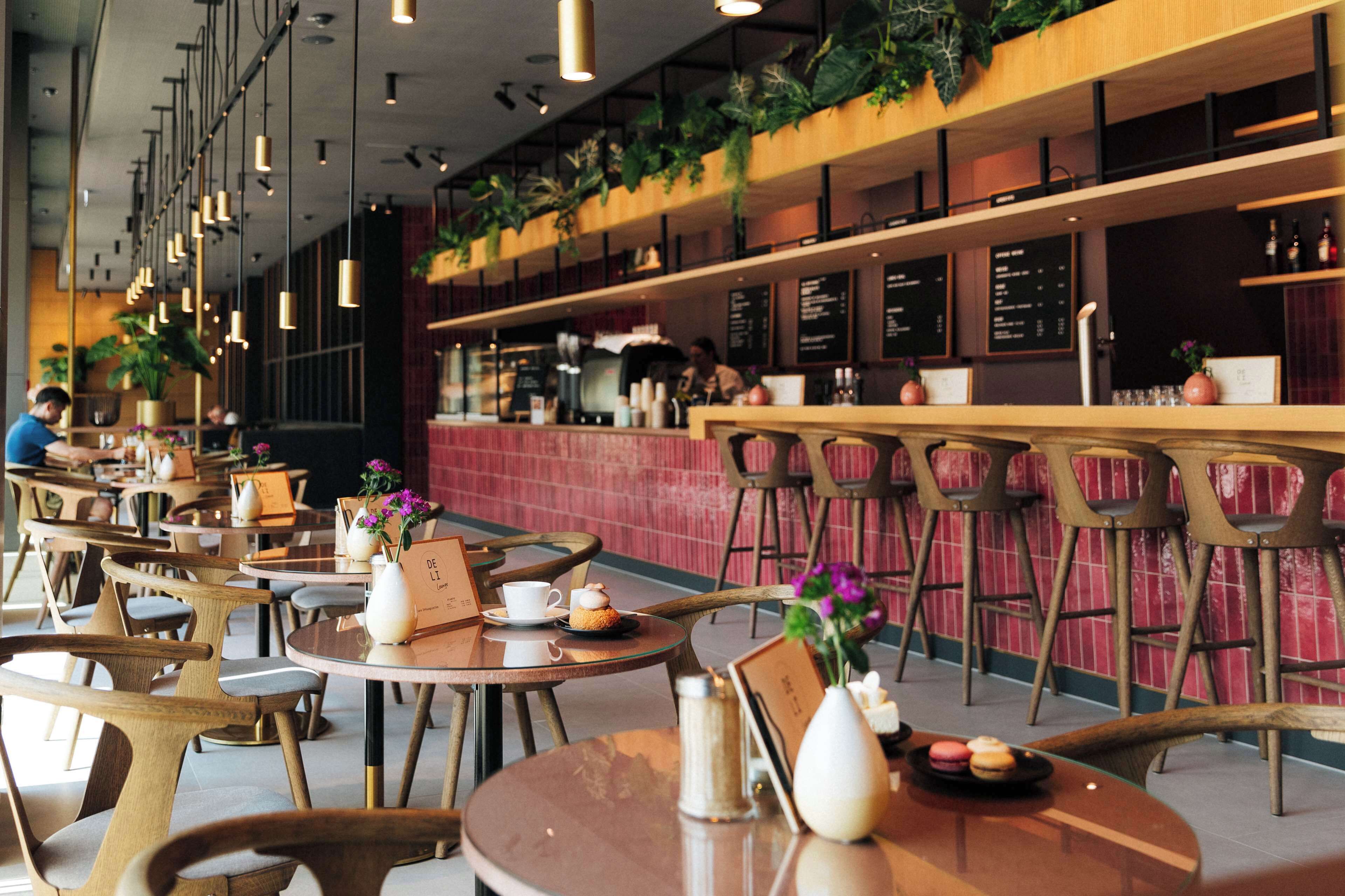 Un café moderno con mesas redondas, sillas y plantas colgantes.