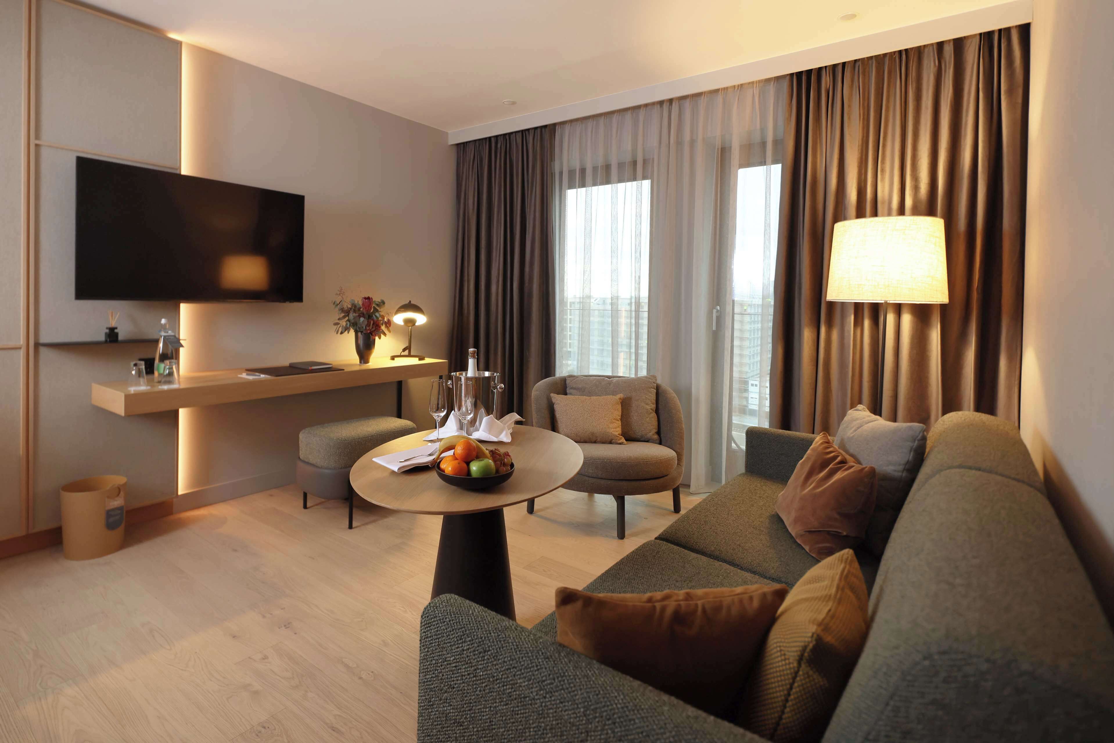 A modern living room with a flat-screen TV, a round coffee table with fruits, a sofa, and a chair.