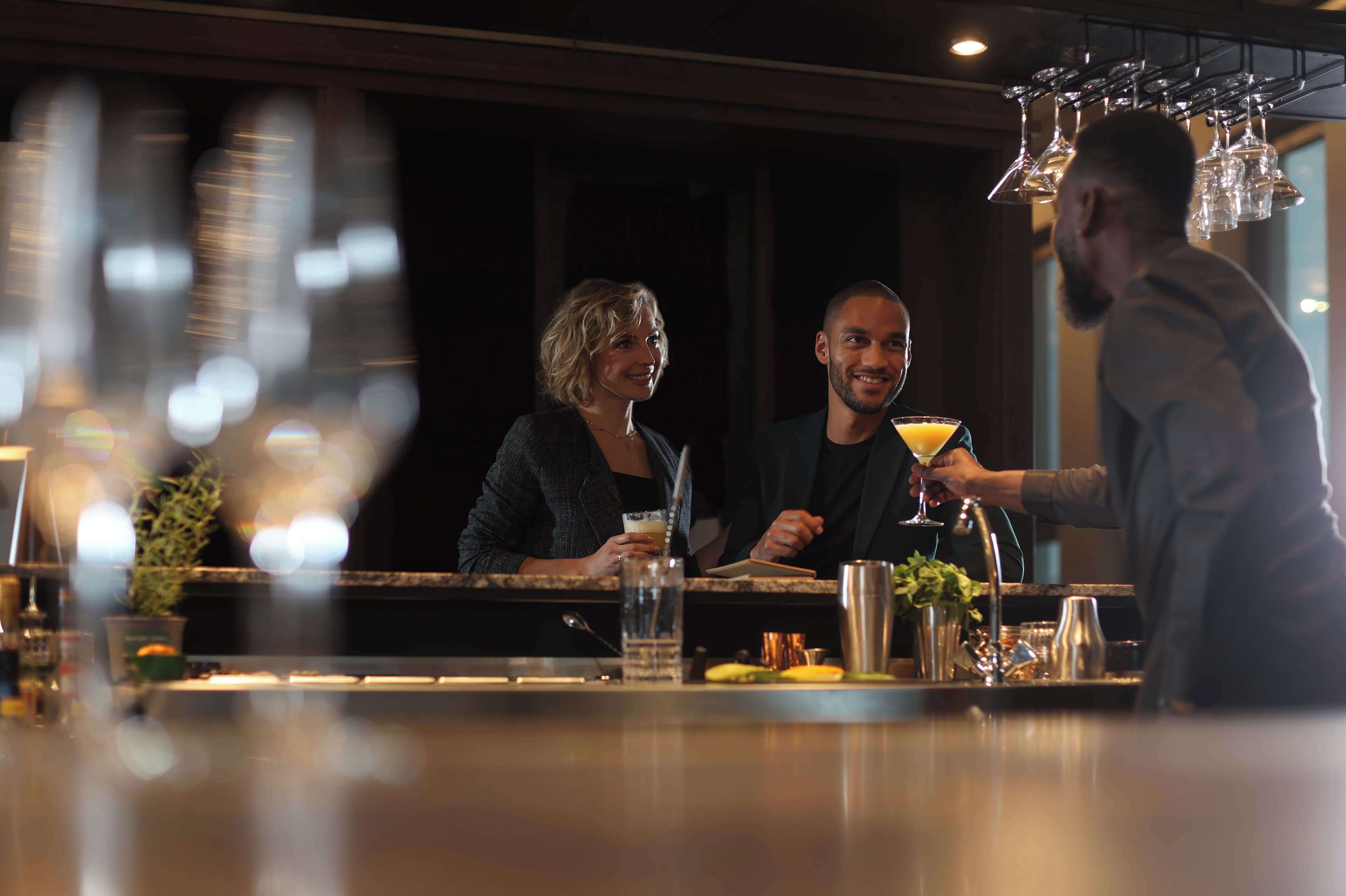 A bar area with a counter, glasses, and a person preparing a drink.