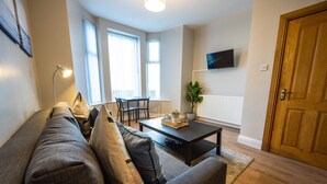 A living room with a sofa, coffee table, and a TV mounted on the wall. - Home Away From Home (Newcastle)