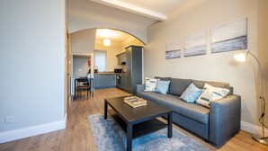 A modern living room with a grey sofa, a dark coffee table, and a kitchen in the background. - Home Away From Home (Newcastle)