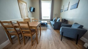 A living room with a wooden dining table, chairs, a sofa, and a television mounted on the wall. - Home Away From Home (Newcastle)
