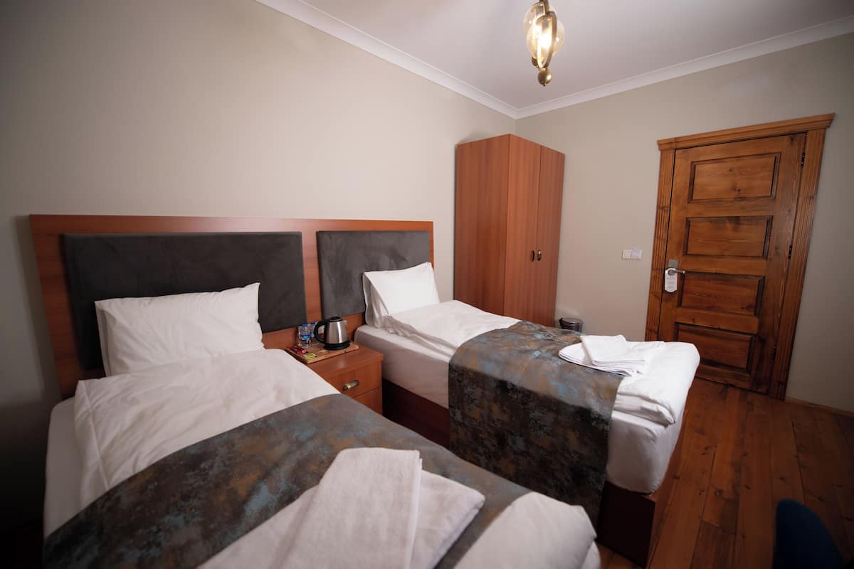 A hotel room with two beds, a wardrobe, a nightstand, and a door.