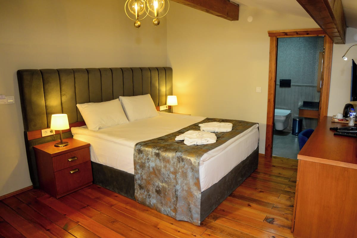 A bedroom with a wooden floor, a bed with white linens, two bedside lamps, and a wooden headboard.