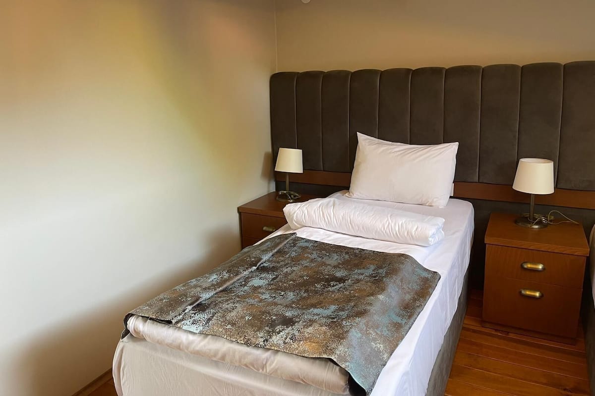 A neatly made bed with a headboard, two bedside tables with lamps, and a wooden floor.