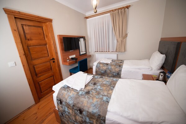 A hotel room with two beds, a wooden door, a mirror, a window with curtains, and a small table with a kettle.