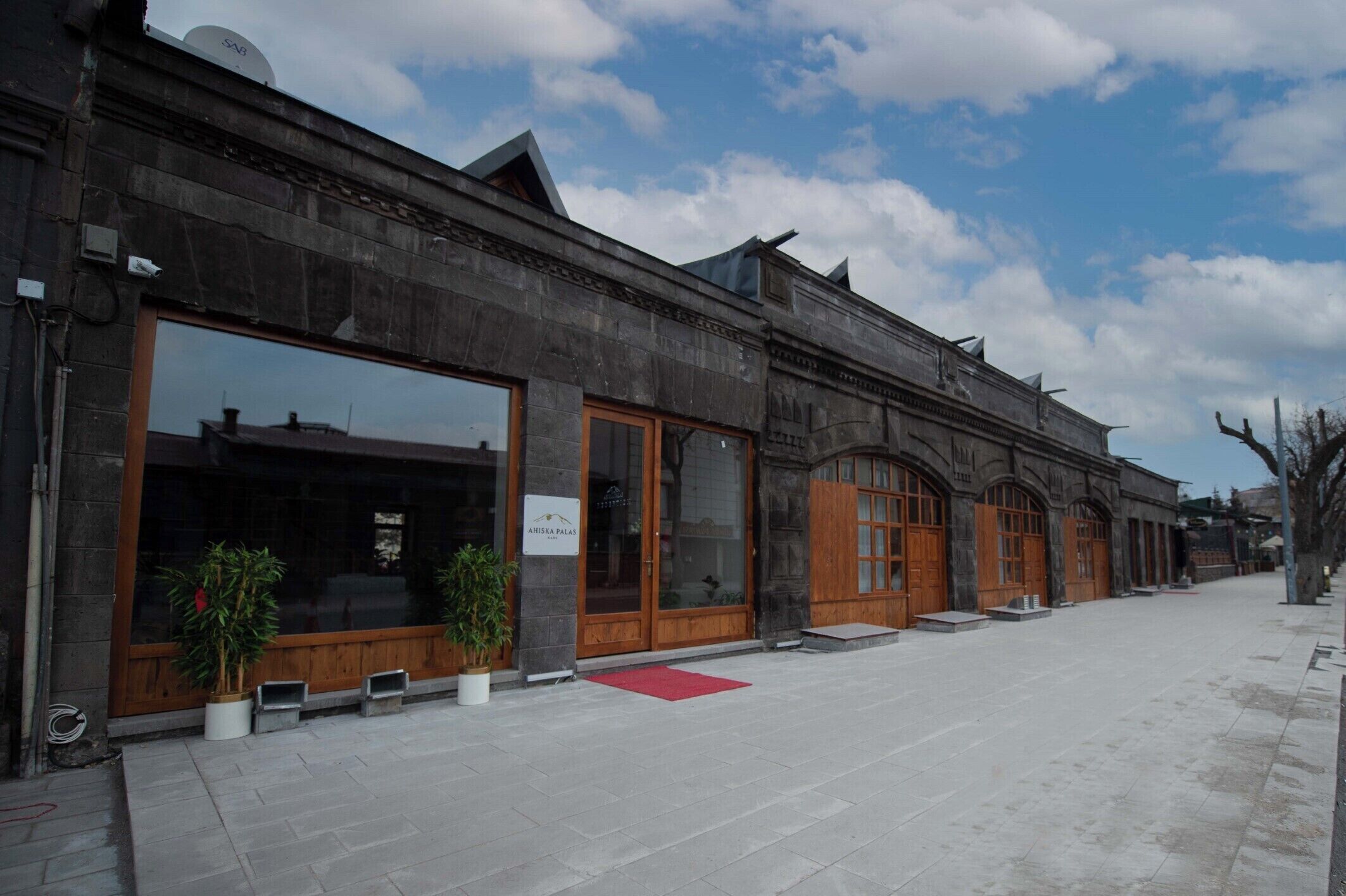 A building with large windows and wooden doors, a red carpet, and potted plants.