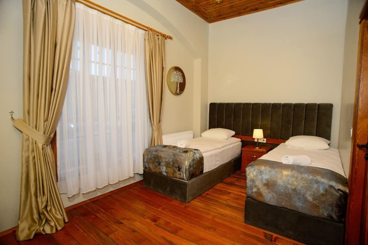 A room with two beds, wooden flooring, and a window with curtains.