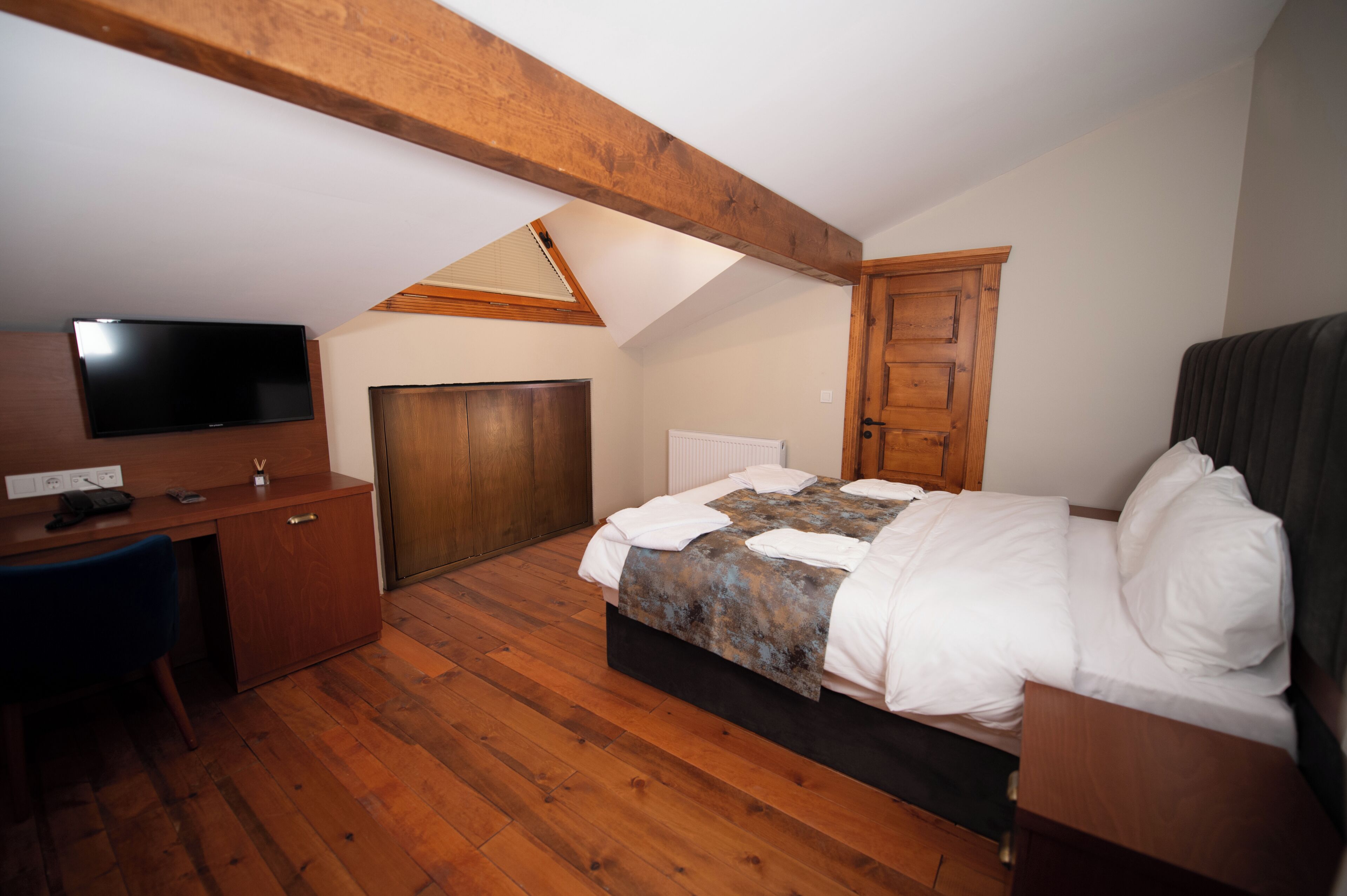 A bedroom with a bed, wooden desk, television, and a sloped ceiling.