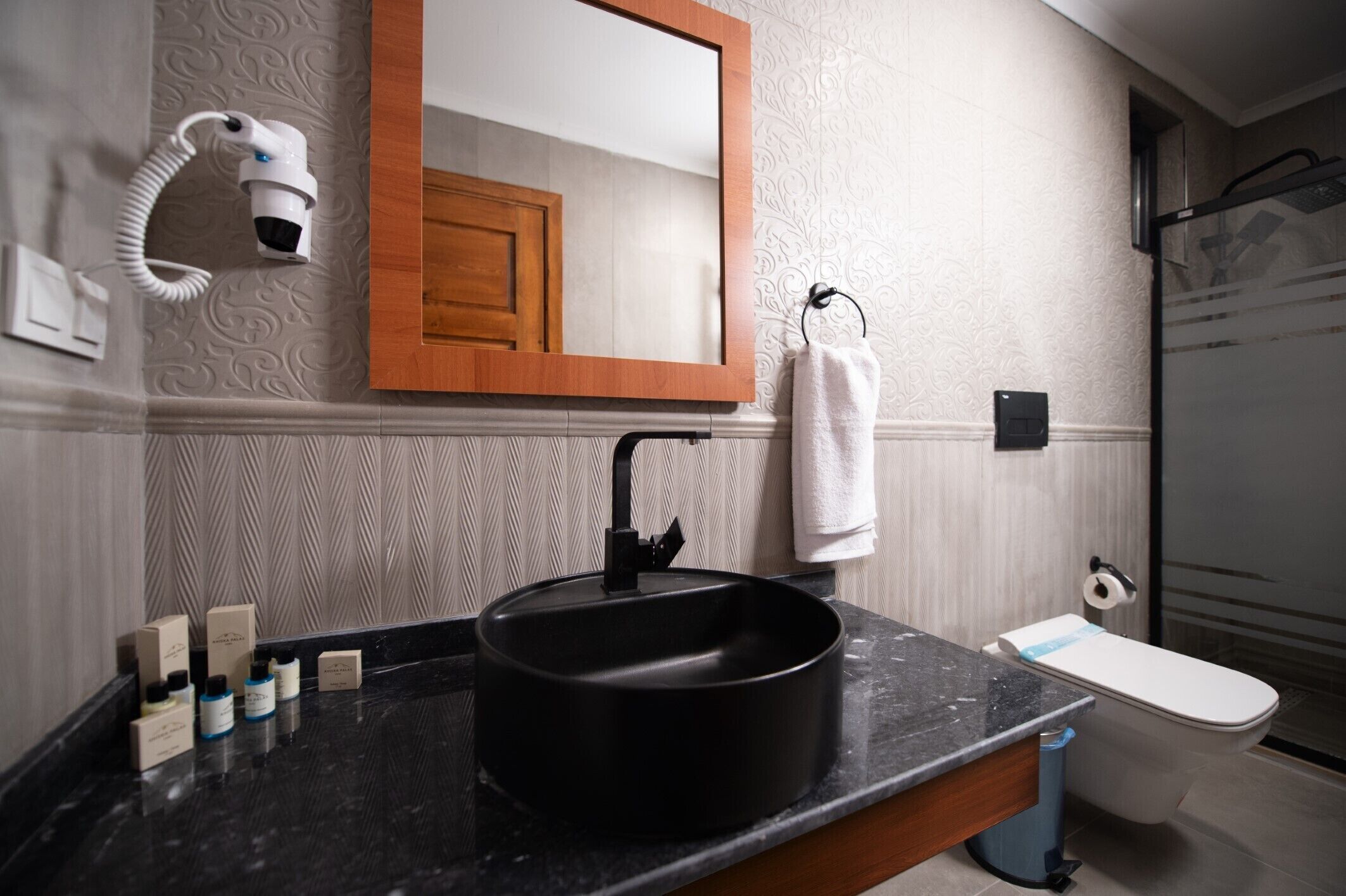 A bathroom with a black sink, a mirror, a towel rack, a toilet, and a hairdryer.