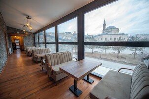 Un restaurante con mesas y bancos de madera, ventanas amplias y vistas a un edificio con cúpula y minarete.
